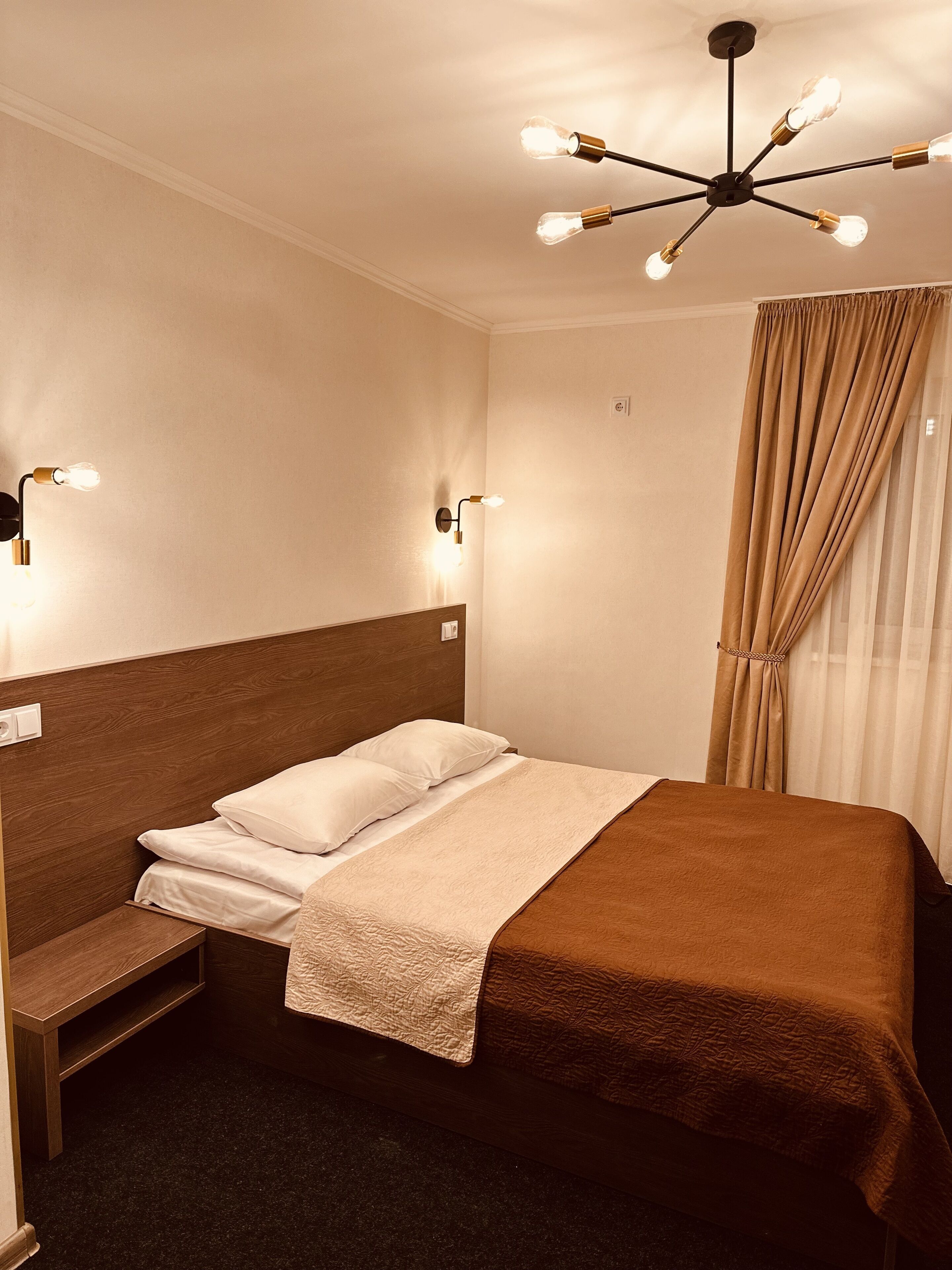 A hotel room with a bed, bedside tables, a ceiling light fixture, and a window with curtains.