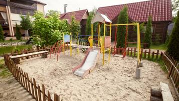A playground with a slide and swings, surrounded by a wooden fence and sand.