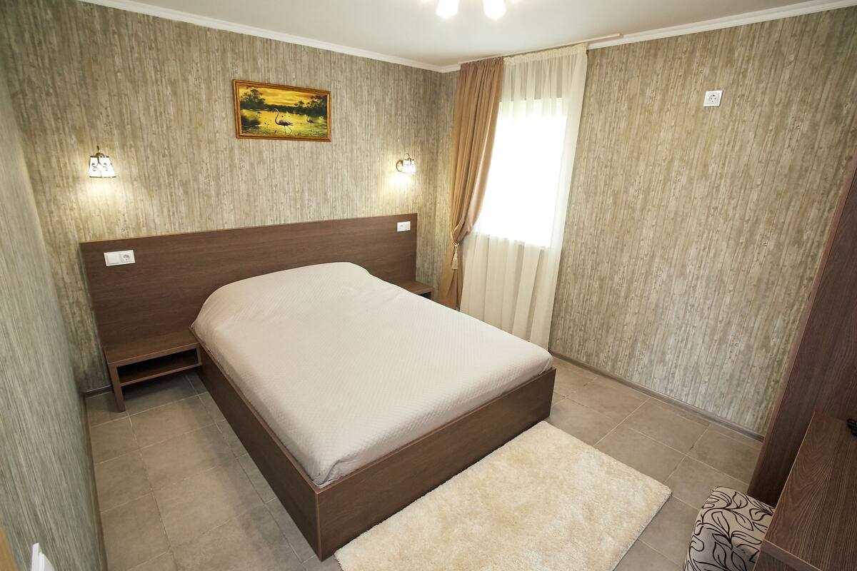 Quarto com cama de madeira, tapete bege e uma pintura na parede.