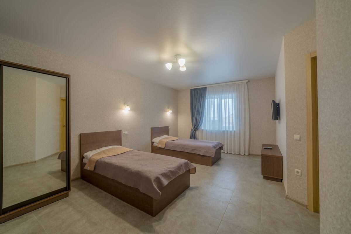Quarto de hotel com duas camas, um espelho grande, mesa de cabeceira e luminária no teto.