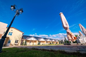 A row of yellow buildings with solar panels, outdoor umbrellas, and a street lamp. - Rayskiy Dvorik (Pohreby)