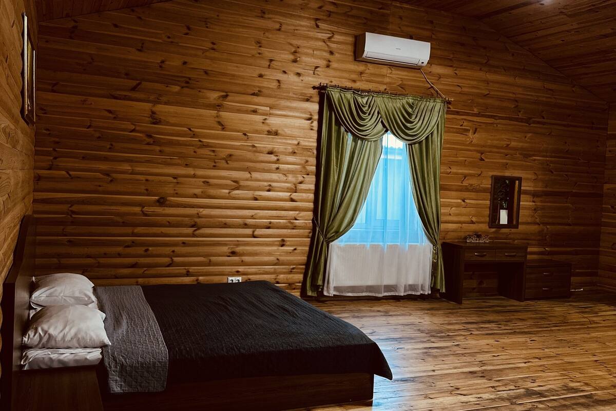 Quarto de cabana de tronco com cama, mesa de cabeceira, cômoda e lustre.