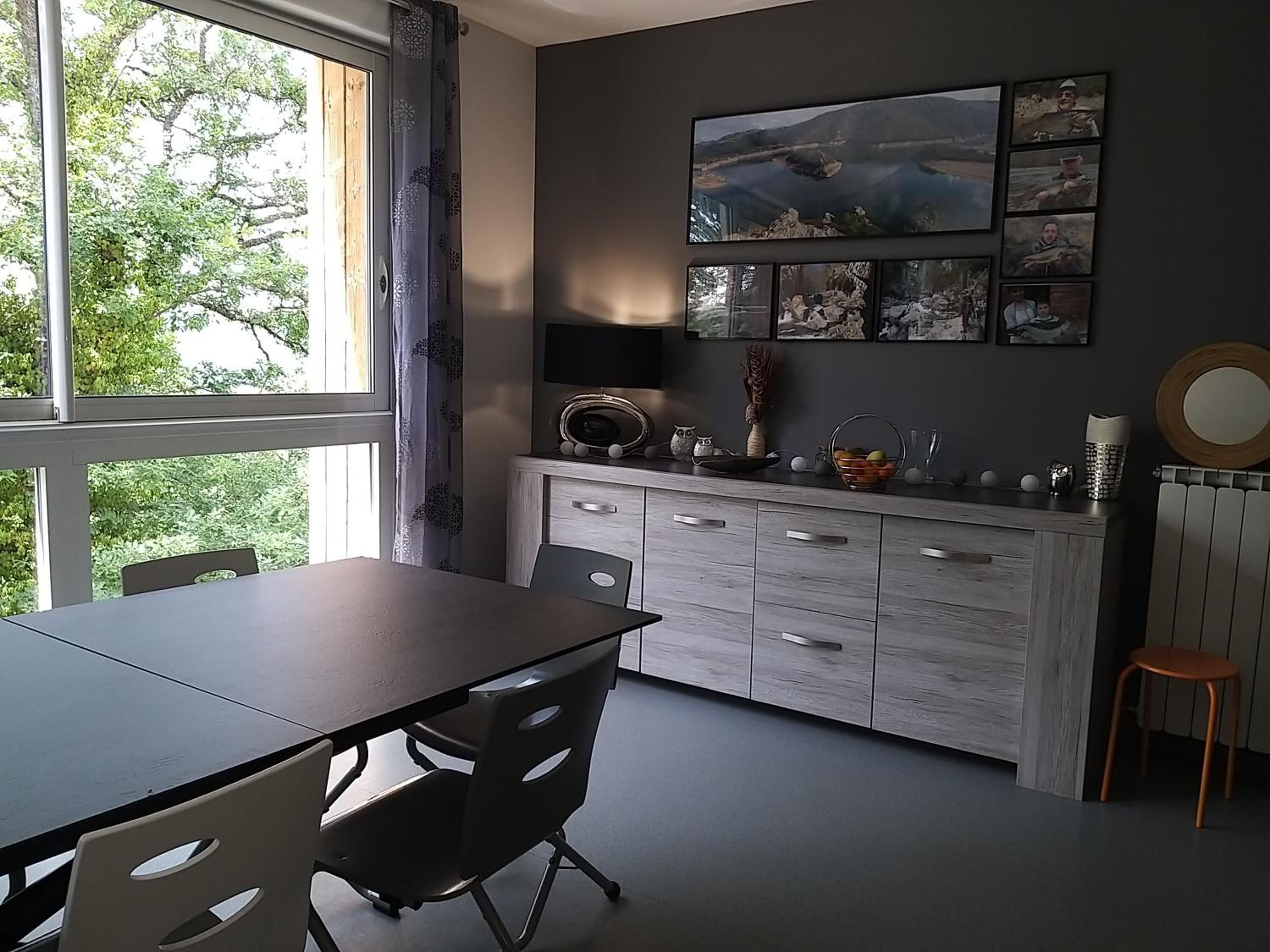 Une cuisine moderne avec une table et des chaises, une grande fenêtre donnant sur les arbres et un téléviseur fixé au mur.