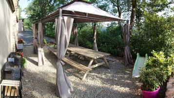 Een overdekt terras met een tafel en stoelen, omringd door grind en groen.