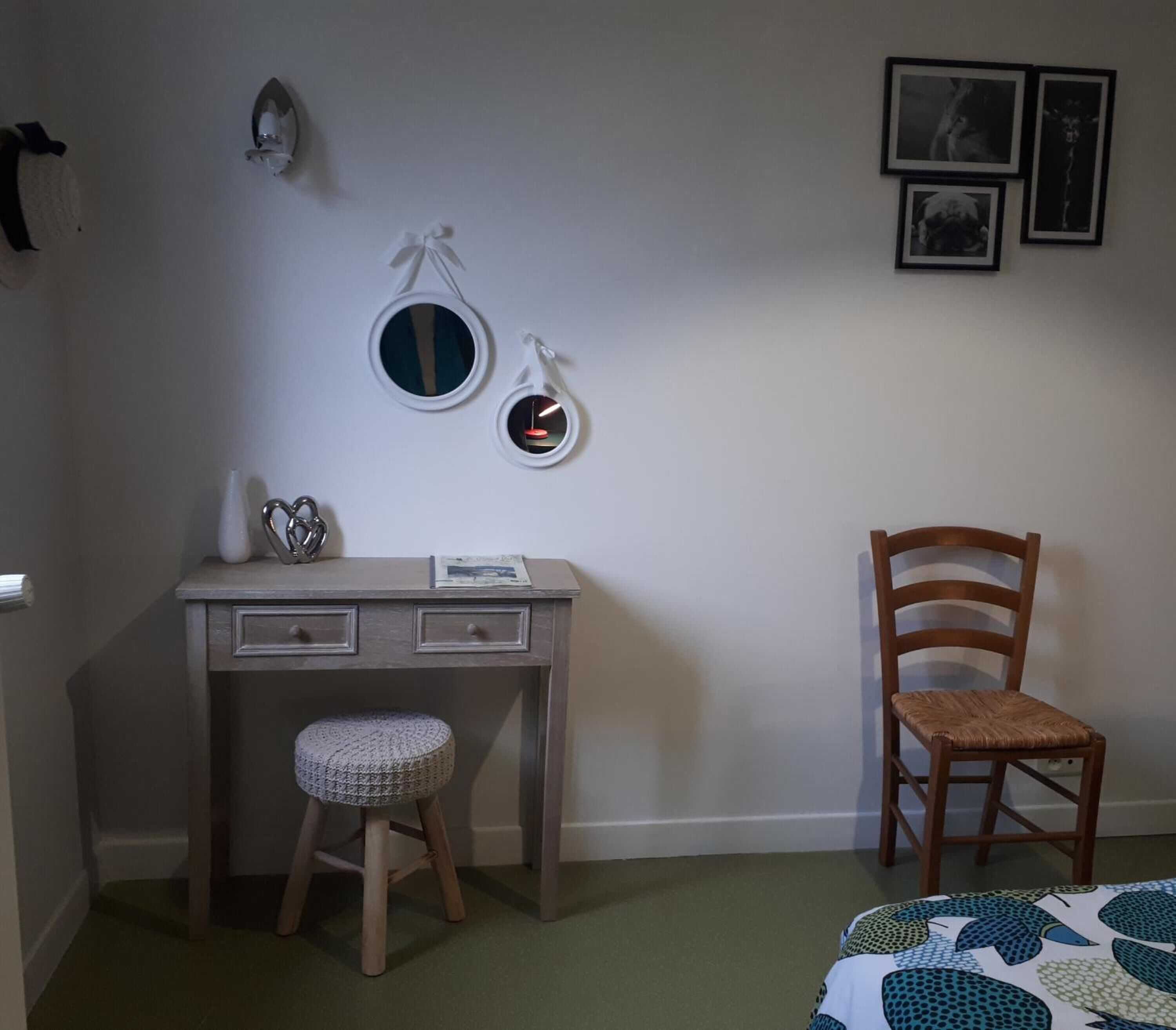 Et værelse med skrivebord, stol, skammel og seng.