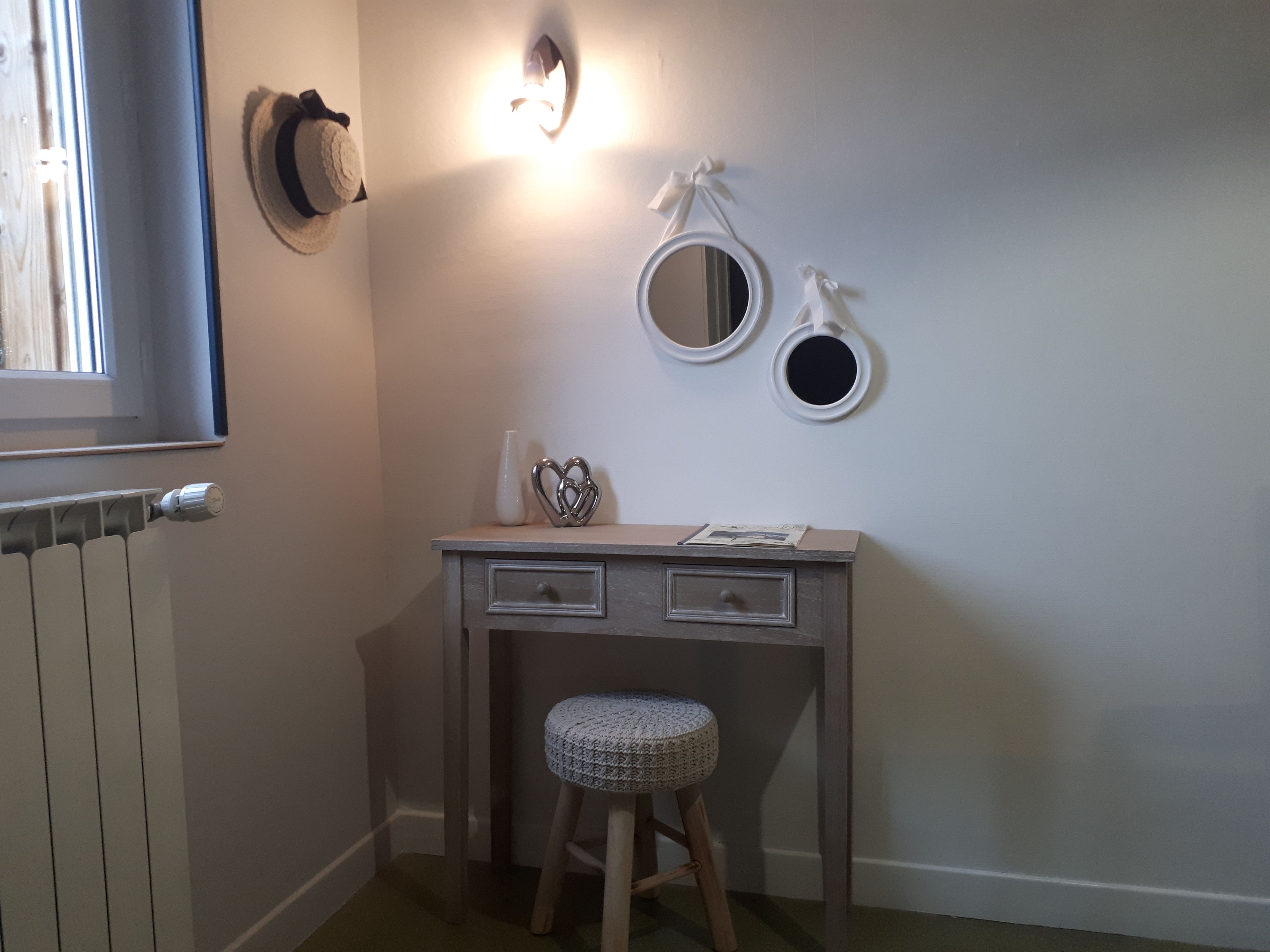 A small, neatly organized bathroom with a radiator, a vanity with two drawers, a stool, and wall-mounted mirrors.