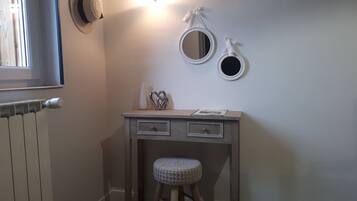 A small, neatly organized bathroom with a radiator, a vanity with two drawers, a stool, and wall-mounted mirrors.