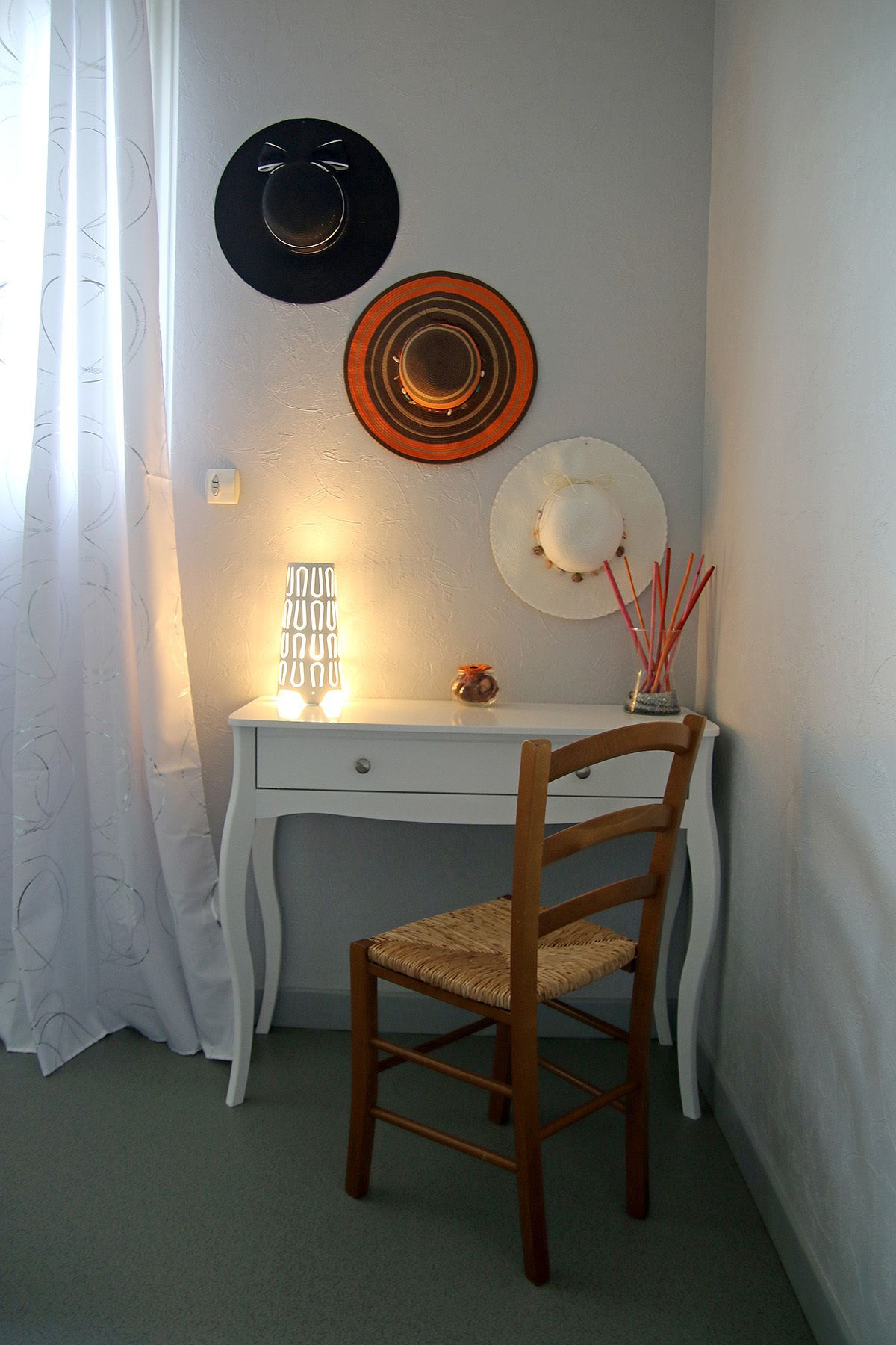 Une pièce d’angle avec un bureau blanc, une chaise en bois et un chapeau accroché au mur.