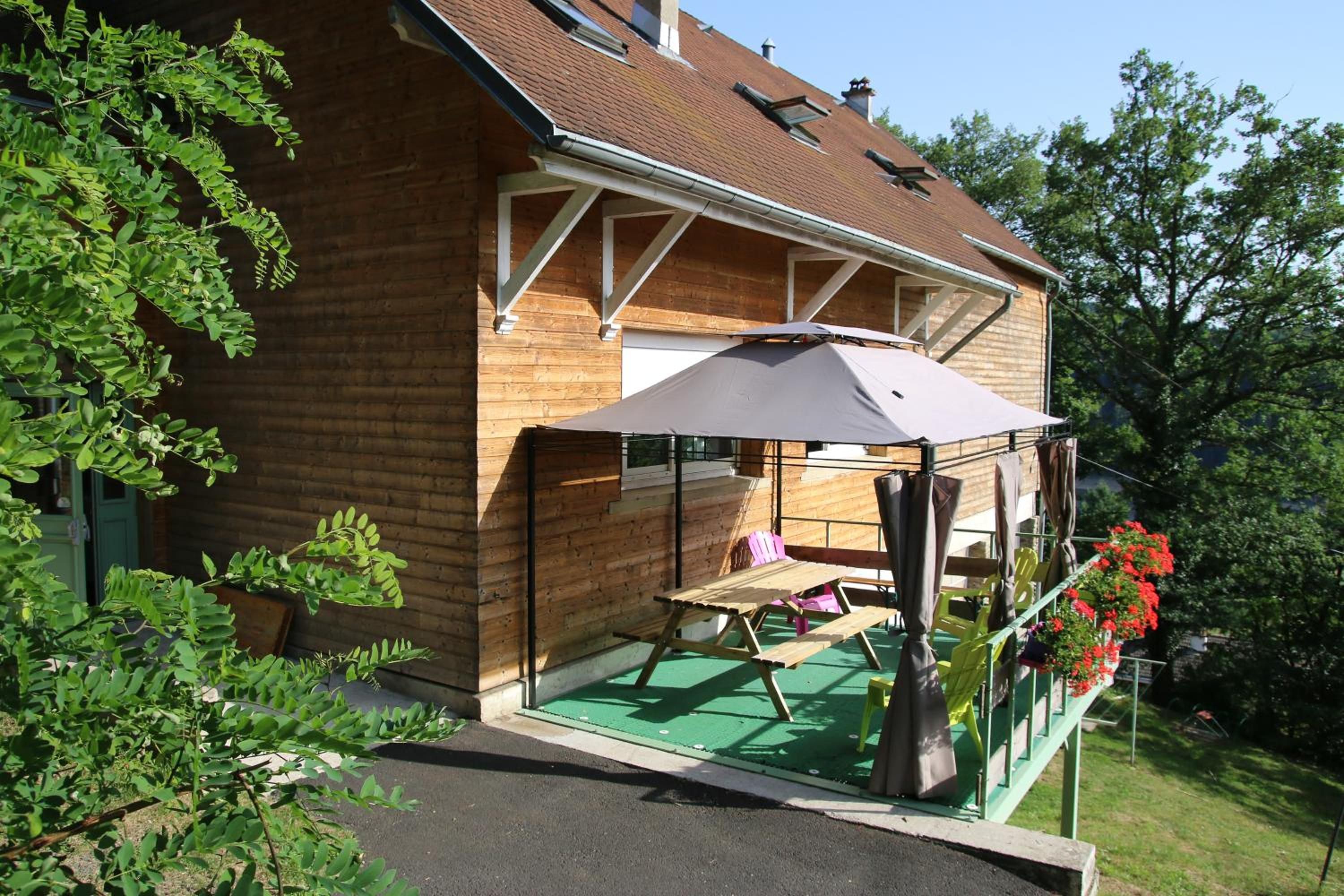 A wooden house with a covered patio area, a green lawn, and a flower bed with red flowers.