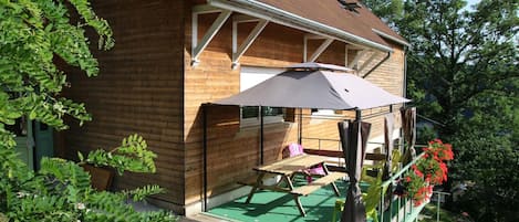 A wooden house with a covered patio area, a green lawn, and a flower bed with red flowers.