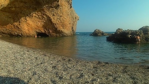 Une plage rocheuse avec une eau claire et une grande formation rocheuse.