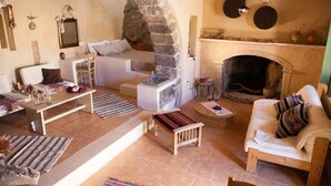 Un salon chaleureux avec une cheminée en pierre, un canapé blanc, un banc en bois et une petite table agrémentée d’objets décoratifs.