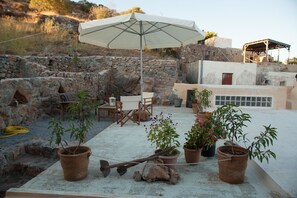 Eine Dachterrasse mit Steinmauern, Gartenmöbeln, Blumentöpfen und einem großen Sonnenschirm.