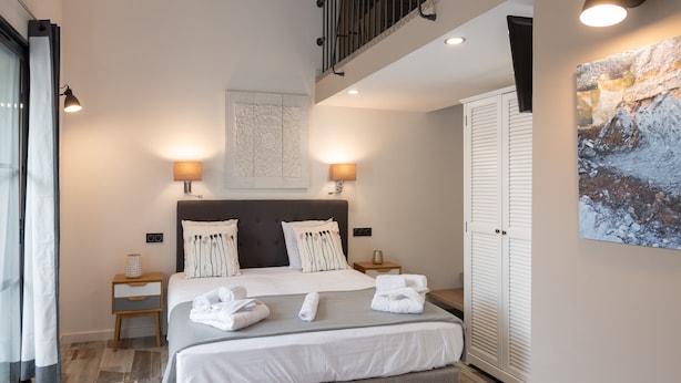A modern bedroom with a large bed, two bedside tables, a headboard with a decorative panel, a ceiling light, a wall-mounted artwork, and a wardrobe. - Casa di a Restonica (Corte)