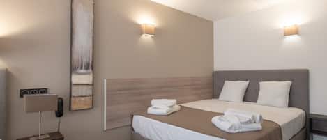 A modern hotel room with a large bed, two bedside lamps, a painting on the wall, and a small bedside table with a lamp.