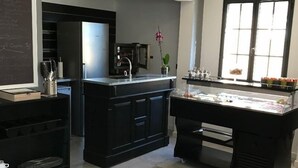 A modern kitchen with black cabinetry, a stainless steel refrigerator, a built-in oven, and a glass display case with food items. - Casa di a Restonica (Corte)