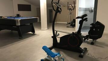 Una habitación con mesa de billar, equipo de ejercicio y puerta que da a un baño.
