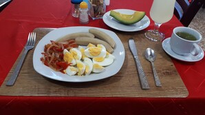 Uma mesa posta com um prato de ovos, bananas e cebolas, um copo de bebida gelada com limão e uma xícara de chá.