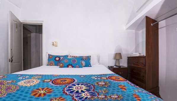 A bedroom with a bed, two pillows, a nightstand, a lamp, and a wooden wardrobe.