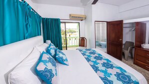 Quarto de hotel com cama, uma cadeira, guarda-roupa e varanda com vista.