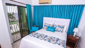 Quarto com cama, mesa de cabeceira, janela com cortinas e vista para o exterior.