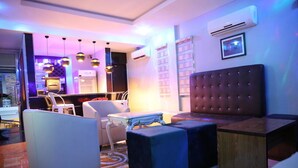 A modern living room with a tufted headboard, a white armchair, a small white table, and a blue ottoman. - Kiniz Luxury Apartments (Uyo)