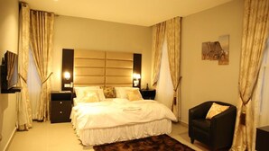 A bedroom with a large bed, two bedside tables, a chair, and a headboard with built-in lighting. - Kiniz Luxury Apartments (Uyo)