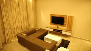 A living room with a sectional sofa, a flat-screen TV, and a coffee table. - Kiniz Luxury Apartments (Uyo)