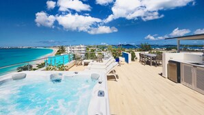 A rooftop terrace with a hot tub, lounge chairs, and a view of the beach and ocean.