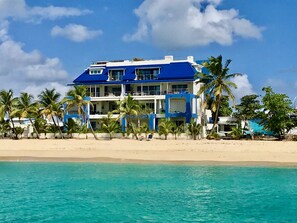 Un hotel frente al mar con varios balcones, palmeras y vista despejada del océano.