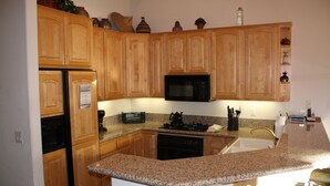 Une cuisine avec des meubles de rangement en bois, un plan de travail en granit, un four à micro-ondes encastré et une cuisinière.