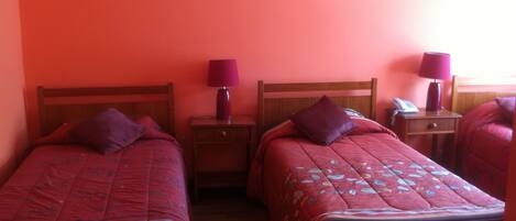 A room with two single beds, each with a wooden headboard, a bedside table, a lamp, and a telephone.