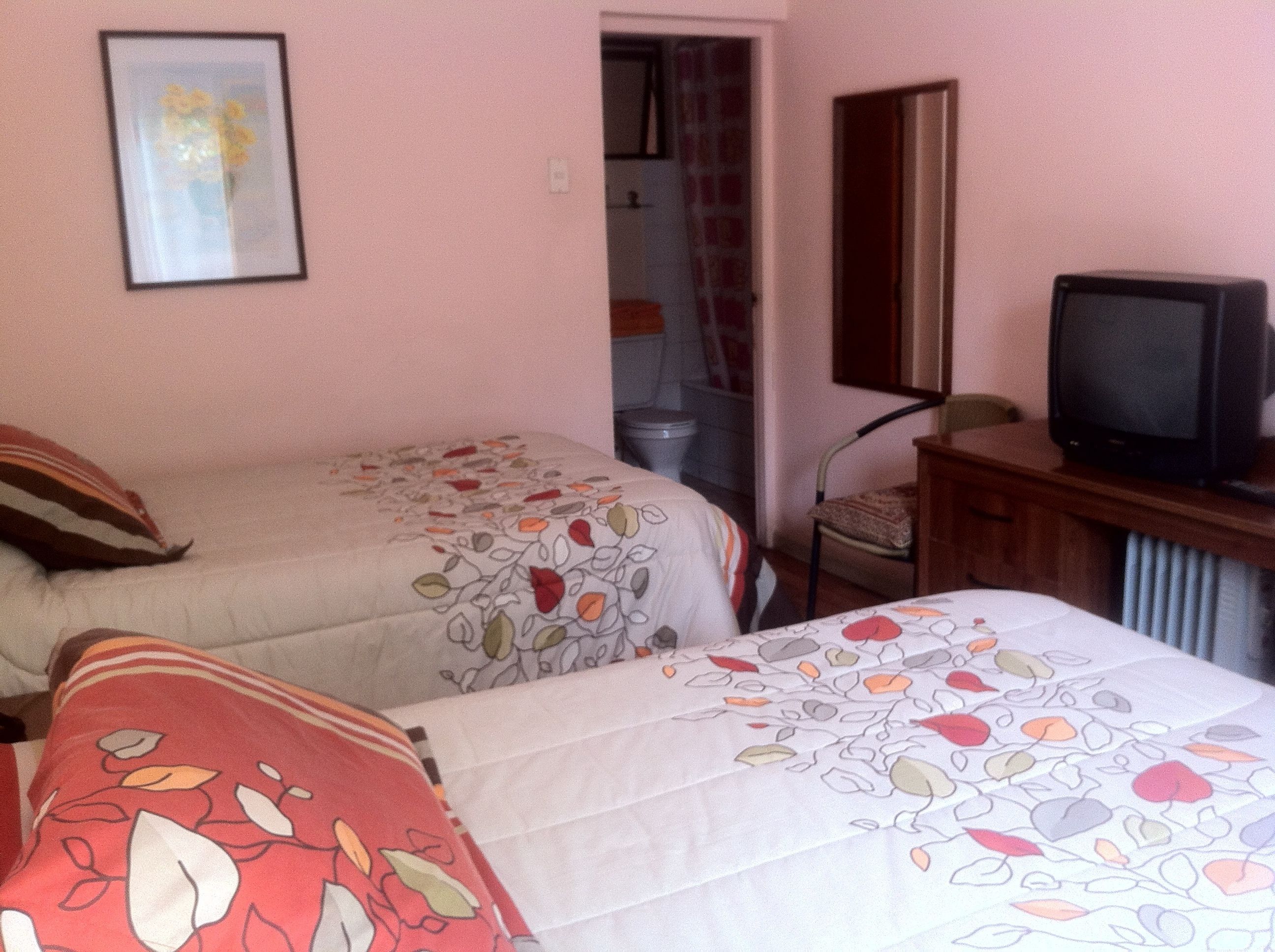 Un dormitorio con dos camas, un televisor y un baño visible a través de una puerta abierta.