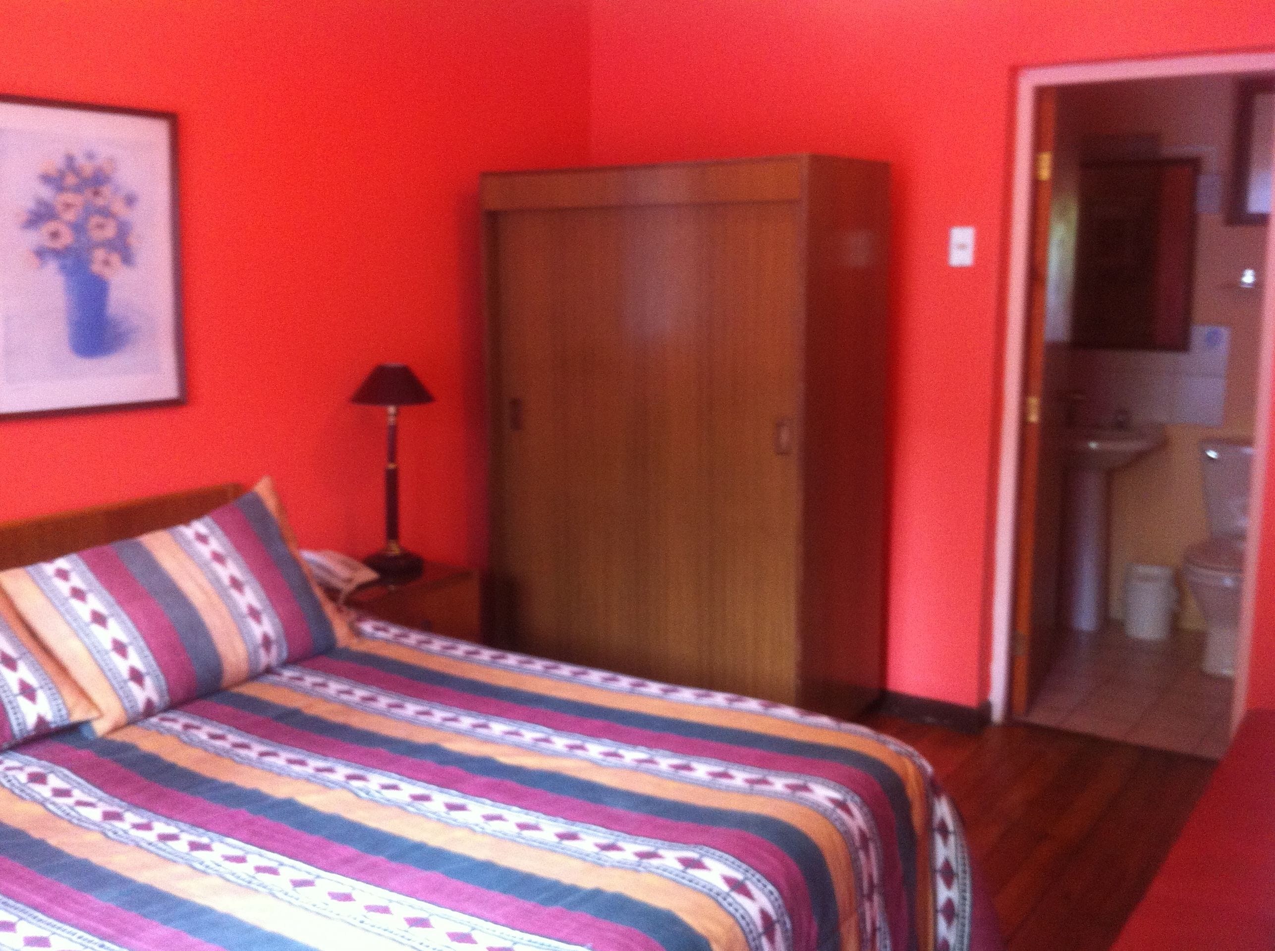 Una habitación con cama, armario, lámpara y baño visible a través de una puerta abierta.