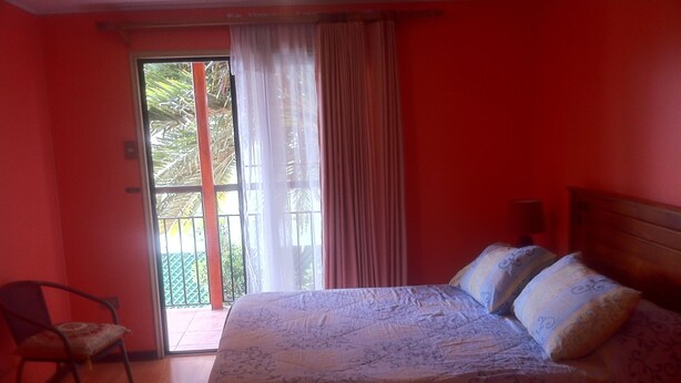 Un dormitorio con cama, una silla y ventana con cortinas.