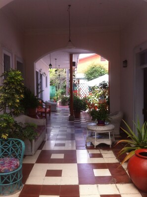 A covered corridor with checkered flooring, potted plants, and wicker furniture. - Hotel del Cid (La Serena)