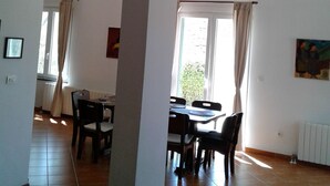 A spacious room with a high ceiling, exposed wooden beams, a dining area with a table and chairs, and a large window with curtains. -  Home in Serene Village-Vineyards Views-Central To All Attractions-Highway   (Zemunik Gornji)