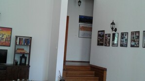 A spacious living area with a wooden staircase leading to a second floor, a sofa, a bookshelf, and framed pictures on the walls. -  Home in Serene Village-Vineyards Views-Central To All Attractions-Highway   (Zemunik Gornji)