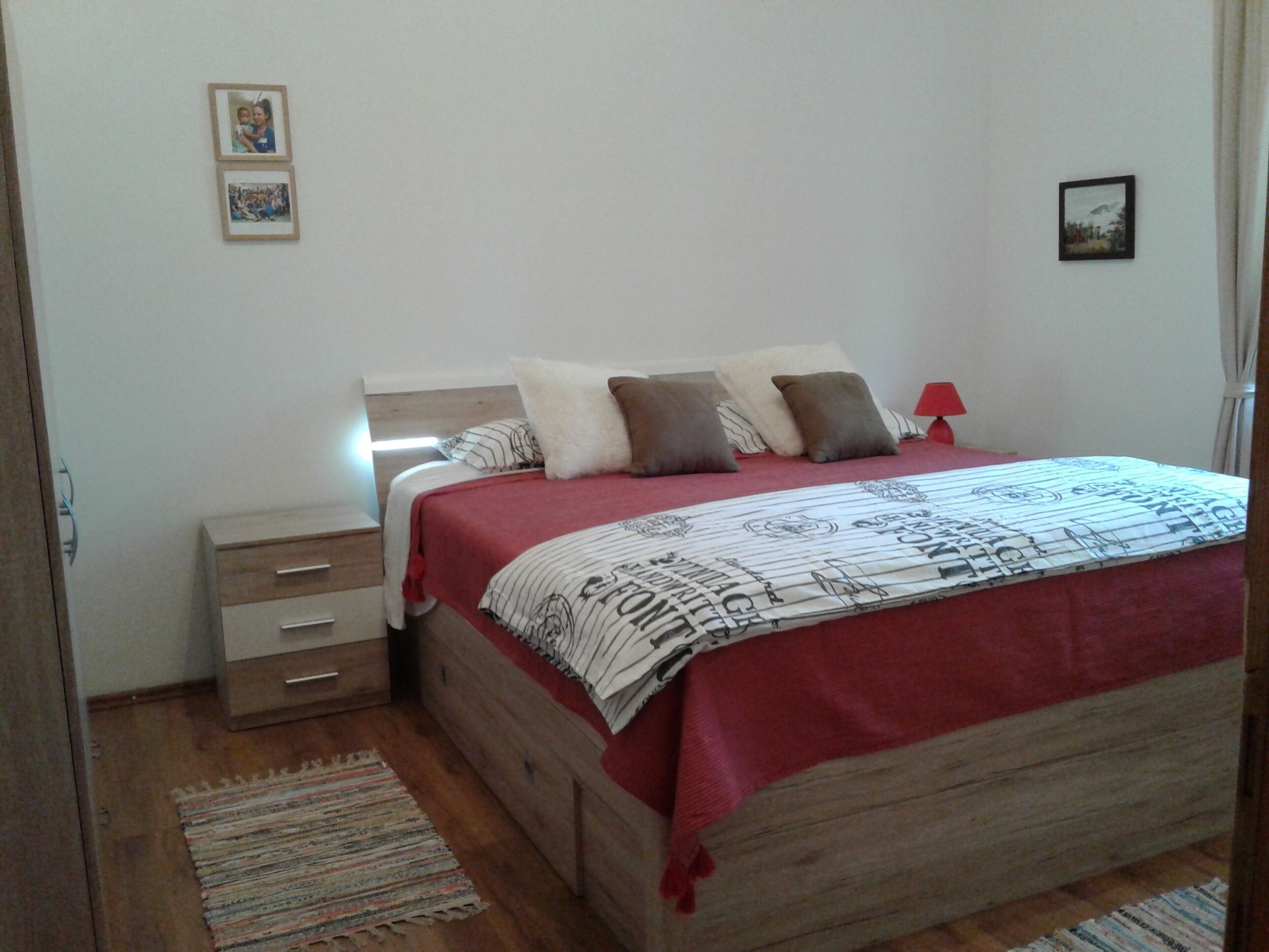 Una camera da letto con un letto in legno, un comodino e una lampada rossa.