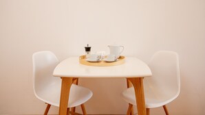 A table with two white chairs, a tray with a teapot, cups, and a small black object.