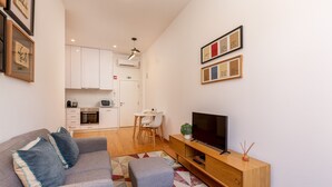 A modern living room with a sofa, ottoman, TV, and a small table with a plant.