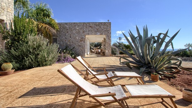 A stone building with a patio area featuring lounge chairs and potted plants.