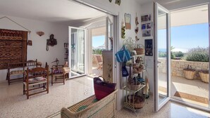 A spacious living area with a large open door leading to a balcony, wicker furniture, and various decorative items on the walls.