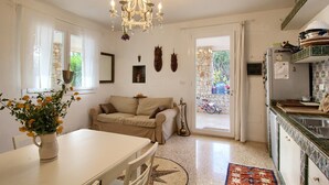 A compact living space with a dining area, a sofa, a chandelier, and a kitchen with a tiled backsplash.