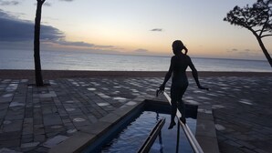 A person standing on a metal railing overlooking a body of water, with a paved walkway and trees in the background. - CALA DEL PI RESIDENTIAL APARTMENT (TREUMAL CENTER) PLATJA D¨ARO (Platja D Aro)