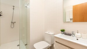 Et moderne badeværelse med et glasafskærmet brusebad, et hvidt toilet og et håndvaskarrangement med spejl, vask og dekorative genstande.