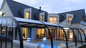 A modern house with a covered swimming pool area, large windows, and a well-lit interior. - DOËLAN, Villa ***** 12 p, heated indoor pool, spa, sauna, billiards (Clohars-Carnoët)
