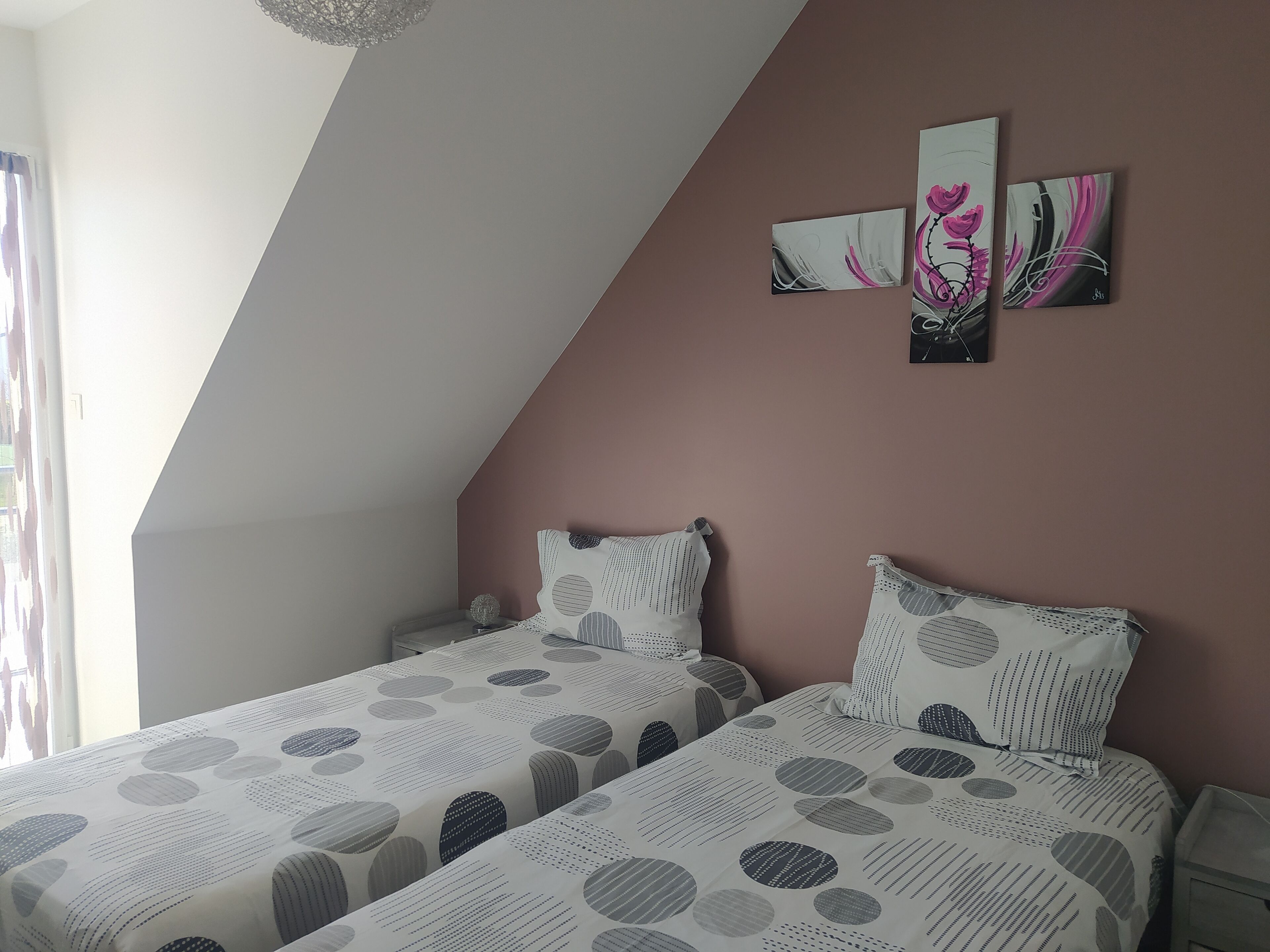 Une chambre avec deux lits, un mur d’accent de couleur rose et un luminaire au plafond.