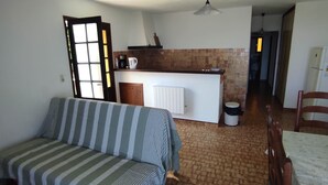 Ein Wohnzimmer mit einem gestreiften Sofa, einem Esstisch mit Stühlen und einer Küchenzeile mit Kühlschrank sowie gefliestem Rücksprung.