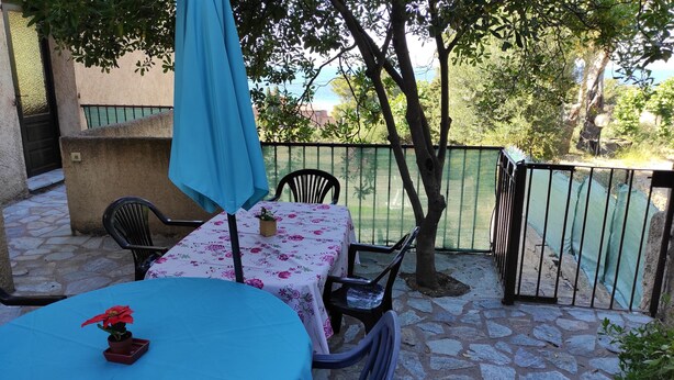Eine Terrassenanlage im Freien mit Tisch und Stühlen, einem blauen Sonnenschirm und Blick aufs Meer.